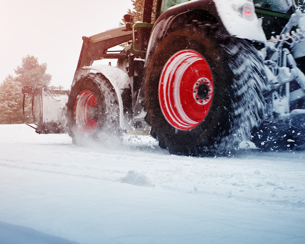 Landmaschine fährt bei Schnee auf Straße
